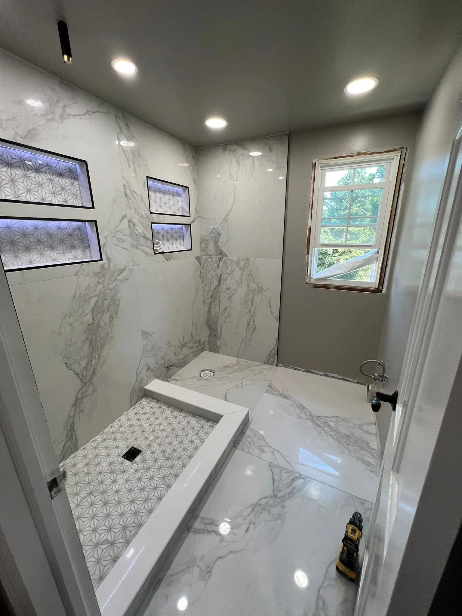 Finished bathroom with marble-look porcelain walls and lit niches